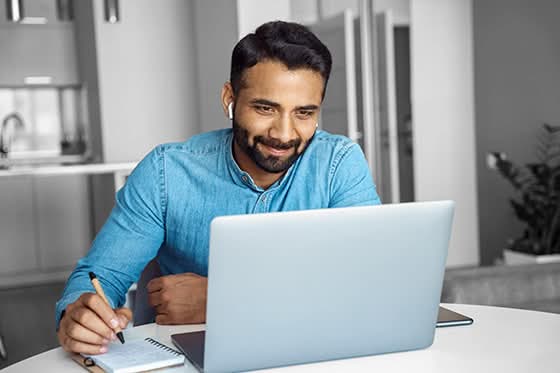 Smiling man in denim shirt taking notes during a virtual meeting