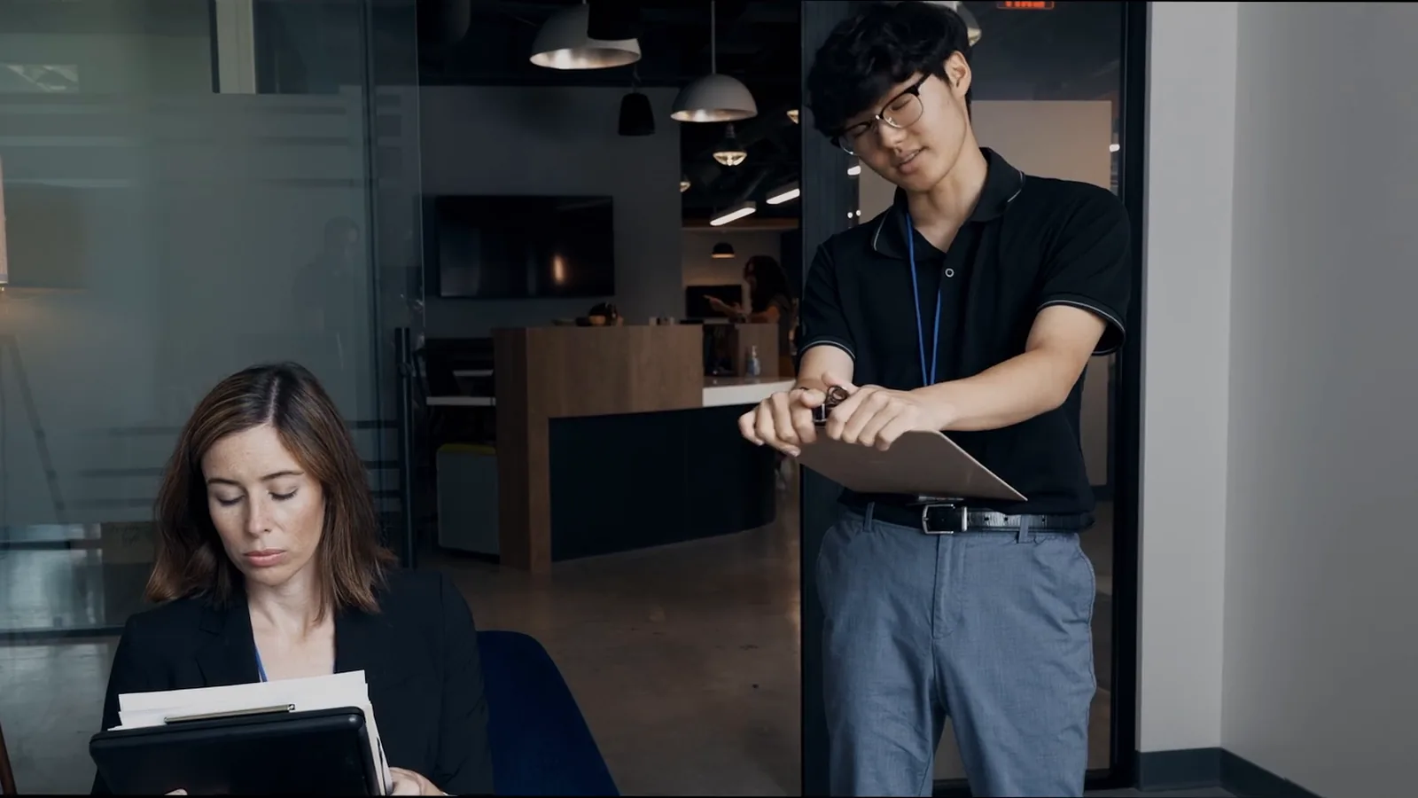 A colleague hands over a clipboard while a manager works through papers in the office.